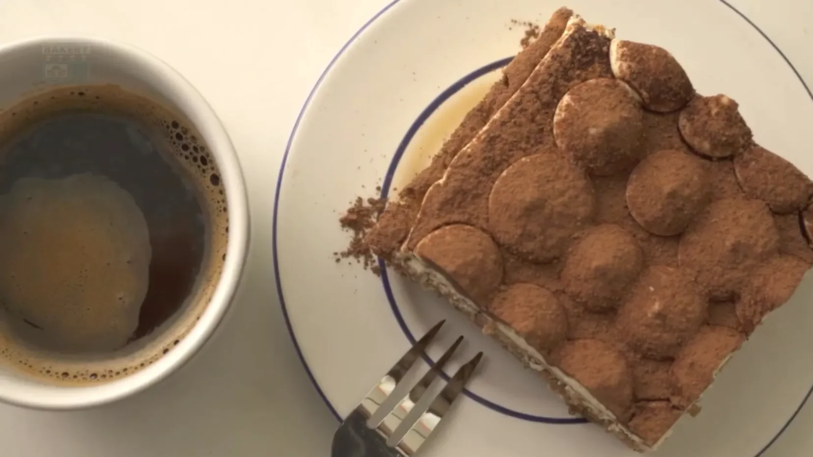 Portion de tiramisu servie sur une assiette blanche avec une fourchette et une tasse de café