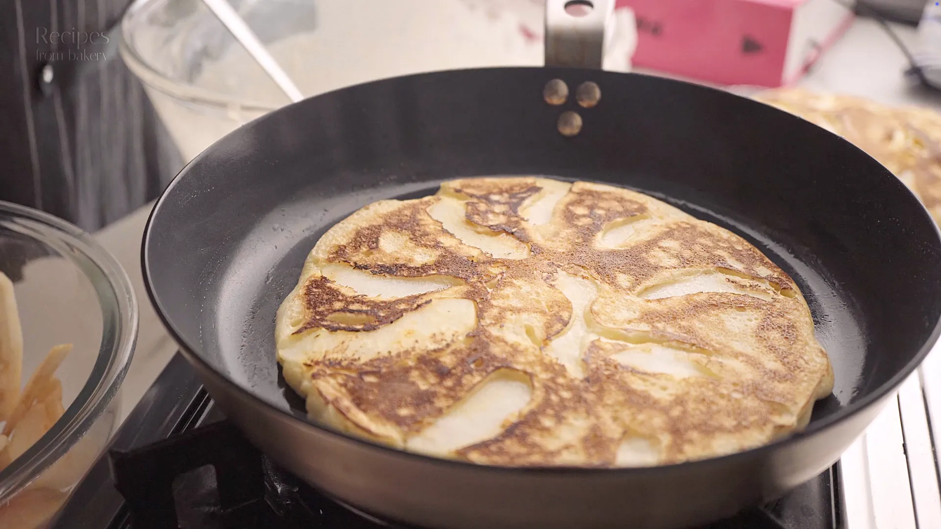 Pancake qui cuit dans une poêle avec tranches de pomme sur le dessus